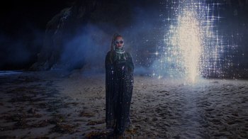 Movie still from “Black Is King” (2020), directed by Julian Klincewicz – A person standing on the beach with fireworks in the background; Wide shot, High angle