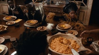 Movie still from “Black Is King” (2020), directed by Julian Klincewicz – A group of people sitting at a table with plates of food; Medium shot, Over the shoulder angle