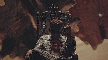 Movie still from “Black Is King” (2020), directed by Julian Klincewicz – A man sitting in a chair with a crown on his head; Medium shot, Low angle