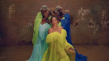 Movie still from “Black Is King” (2020), directed by Julian Klincewicz – A woman sitting in front of two other women in dresses; Extreme Wide shot, High angle