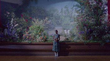 Movie still from “Black Is King” (2020), directed by Julian Klincewicz – A woman standing in front of a painting of a garden; Extreme Wide shot, High angle