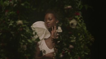 Movie still from “Black Is King” (2020), directed by Julian Klincewicz – A woman in a white dress standing next to a bush; Close Up shot, Over the shoulder angle