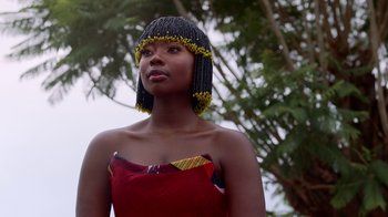 Movie still from “Black Is King” (2020), directed by Julian Klincewicz – A woman in a red and black dress with a black and yellow headdress; Close Up shot, Low angle