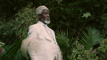 Movie still from “Black Is King” (2020), directed by Julian Klincewicz – An older man in a white suit standing next to a tree; Medium shot, Low angle