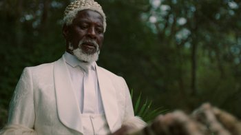 Movie still from “Black Is King” (2020), directed by Julian Klincewicz – An older man wearing a white hat and a white robe; Close Up shot, Low angle