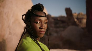 Movie still from “Black Is King” (2020), directed by Julian Klincewicz – A woman with a green shirt and braids on her head; Close Up shot, Low angle