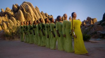 Movie still from “Black Is King” (2020), directed by Julian Klincewicz – A group of women in long green dresses standing next to each other in front of a rock formation; Extreme Wide shot, Low angle