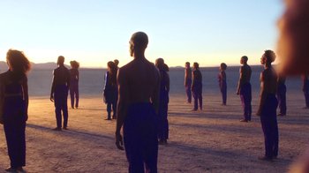 Movie still from “Black Is King” (2020), directed by Julian Klincewicz – A group of people standing on top of a sandy beach; Wide shot, High angle