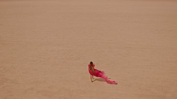 Movie still from “Black Is King” (2020), directed by Julian Klincewicz – A woman in a pink dress is standing in the sand; Extreme Wide shot, Overhead angle
