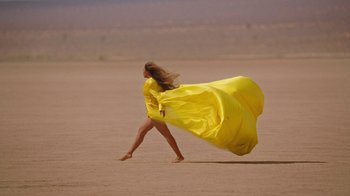 Movie still from “Black Is King” (2020), directed by Julian Klincewicz – A woman walking in the sand with a yellow dress on; Extreme Wide shot, Low angle