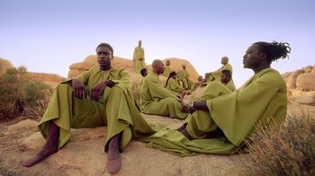 Movie still from “Black Is King” (2020), directed by Julian Klincewicz – A group of men sitting on top of a rock; Wide shot, Low angle