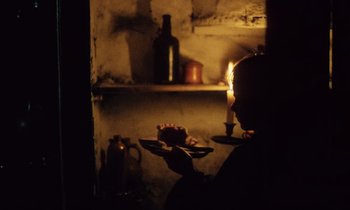 Movie still from “Black Jack” (1979), directed by Ken Loach – A person holding a plate of food in front of a shelf; Medium shot, Over the shoulder angle