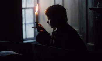 Movie still from “Black Jack” (1979), directed by Ken Loach – A boy is holding a lit candle in a dark room; Medium shot, Over the shoulder angle