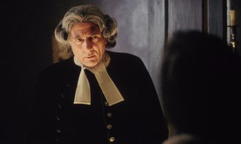 An older man in a wig looking at a mirror