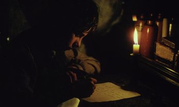 Movie still from “Black Jack” (1979), directed by Ken Loach – A person sitting at a table writing on a piece of paper next to a lit candle; Close Up shot, High angle
