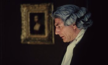 A man in a wig looking down at a painting