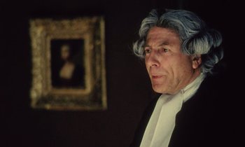 A man in a suit and wig in front of a painting