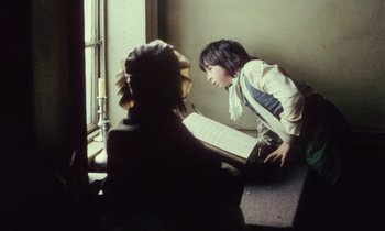 Movie still from “Black Jack” (1979), directed by Ken Loach – Two people sitting in a room looking at a book; Medium shot, Over the shoulder angle