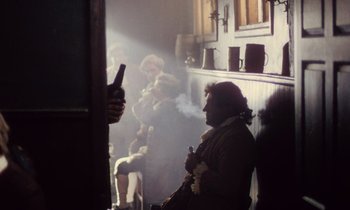 Movie still from “Black Jack” (1979), directed by Ken Loach – A group of people sitting in a room smoking; Medium shot, Over the shoulder angle