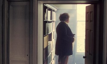 Movie still from “Black Jack” (1979), directed by Ken Loach – A woman standing in front of a book shelf; Wide shot, High angle