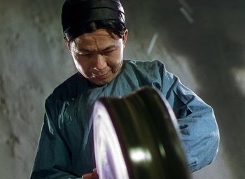 Movie still from “Black Narcissus” (1947), directed by Emeric Pressburger – A man wearing a blue shirt and a black hat is looking at a disc; Medium shot, Low angle