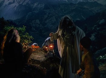 Movie still from “Black Narcissus” (1947), directed by Emeric Pressburger – A man dressed as jesus is standing next to a car; Wide shot, Low angle