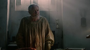 Movie still from “Game of Thrones” (2011), created by D.B. Weiss – An old man with a beard is standing in a room; Medium shot, Over the shoulder angle