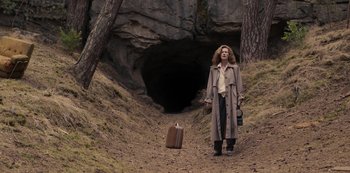 Movie still from “Dark” (2017), created by Baran bo Odar – A woman in a trench coat standing next to a suitcase; Wide shot, High angle
