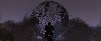 Movie still from “Black Rain” (1989), directed by Ridley Scott – A man riding a motorcycle in front of a globe; Wide shot, Low angle
