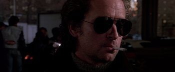 Movie still from “Black Rain” (1989), directed by Ridley Scott – A person wearing sunglasses and smoking a cigarette; Close Up shot, Low angle