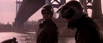 Movie still from “Black Rain” (1989), directed by Ridley Scott – A man in a leather jacket and a motorcycle helmet standing in front of a bridge; Medium shot, Over the shoulder angle