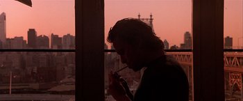 Movie still from “Black Rain” (1989), directed by Ridley Scott – A man smoking a cigarette in front of a window with a city view; Medium shot, Low angle