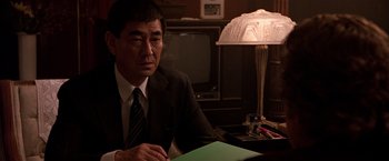 Movie still from “Black Rain” (1989), directed by Ridley Scott – A man sitting at a table in front of a lamp; Close Up shot, Over the shoulder angle