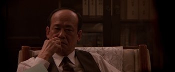 Movie still from “Black Rain” (1989), directed by Ridley Scott – An older man sitting in a chair with his hand under his chin; Close Up shot, Low angle