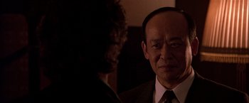 Movie still from “Black Rain” (1989), directed by Ridley Scott – A man standing next to another man wearing a suit; Close Up shot, Over the shoulder angle