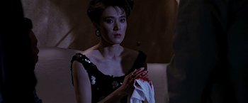 Movie still from “Black Rain” (1989), directed by Ridley Scott – A woman in a black dress holding a white towel; Medium shot, Over the shoulder angle
