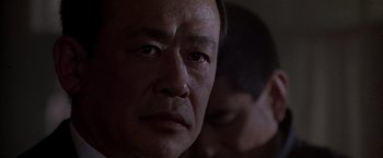 Movie still from “Black Rain” (1989), directed by Ridley Scott – An older man looking at the camera with his eyes closed; Close Up shot, Over the shoulder angle