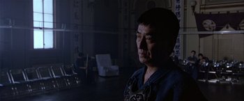 Movie still from “Black Rain” (1989), directed by Ridley Scott – A man standing in the dark in front of a white chair; Medium shot, Low angle