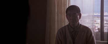 Movie still from “Black Rain” (1989), directed by Ridley Scott – An older asian man standing in front of a window; Medium shot, Low angle