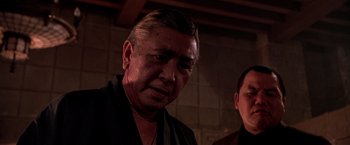 Movie still from “Black Rain” (1989), directed by Ridley Scott – An older man in a black shirt is looking at the camera; Close Up shot, Low angle