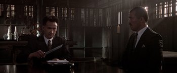 Movie still from “Black Rain” (1989), directed by Ridley Scott – A man sitting at a table in a dark room; Medium shot, Low angle