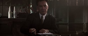 Movie still from “Black Rain” (1989), directed by Ridley Scott – A man sitting at a table in a suit and tie; Close Up shot, Low angle