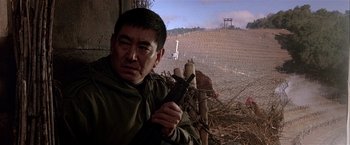 Movie still from “Black Rain” (1989), directed by Ridley Scott – A man holding a rifle in a field; Close Up shot, Low angle