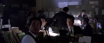 Movie still from “Black Rain” (1989), directed by Ridley Scott – A group of men sitting at a table in a room; Medium shot, Over the shoulder angle