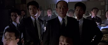 Movie still from “Black Rain” (1989), directed by Ridley Scott – A group of men in suits and ties standing next to each other in a room; Medium shot, Low angle