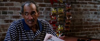 Movie still from “Black Snake Moan” (2006), directed by Craig Brewer – An older man sitting at a table with a stack of papers; Close Up shot, Over the shoulder angle
