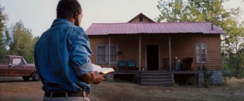 Movie still from “Black Snake Moan” (2006), directed by Craig Brewer – A man is holding something in front of a house; Wide shot, Low angle