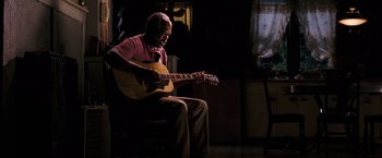 Movie still from “Black Snake Moan” (2006), directed by Craig Brewer – An older man sitting in a chair playing a guitar; Medium shot, Over the shoulder angle