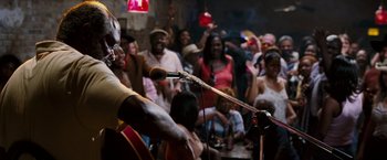 Movie still from “Black Snake Moan” (2006), directed by Craig Brewer – A crowd of people watching a man sing on a microphone; Medium shot, Over the shoulder angle