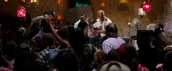 Movie still from “Black Snake Moan” (2006), directed by Craig Brewer – An older man playing guitar in front of an audience; Wide shot, High angle